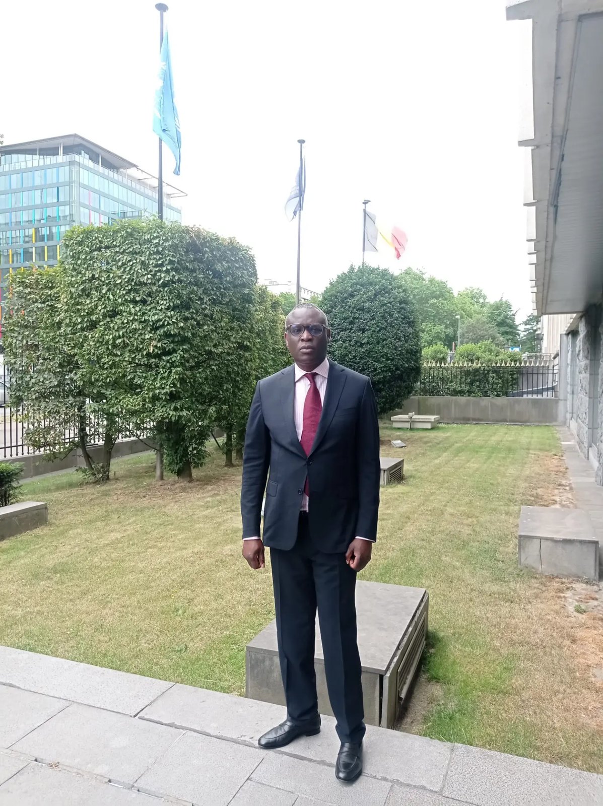 Francis Kibangu devant les mâts portant les drapeaux des Nations Unies et de la Belgique